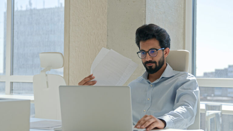 Arabian Indian man tired businessman suffer high temperature uncomfortable heat summer blowing waving papers make wind sit in hot office think project on laptop solve problem broken air conditioner